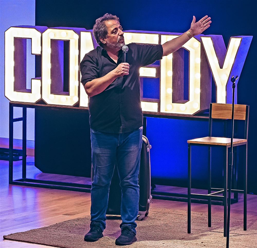 João Seabra em palco, à frente de letras luminosas COMEDY